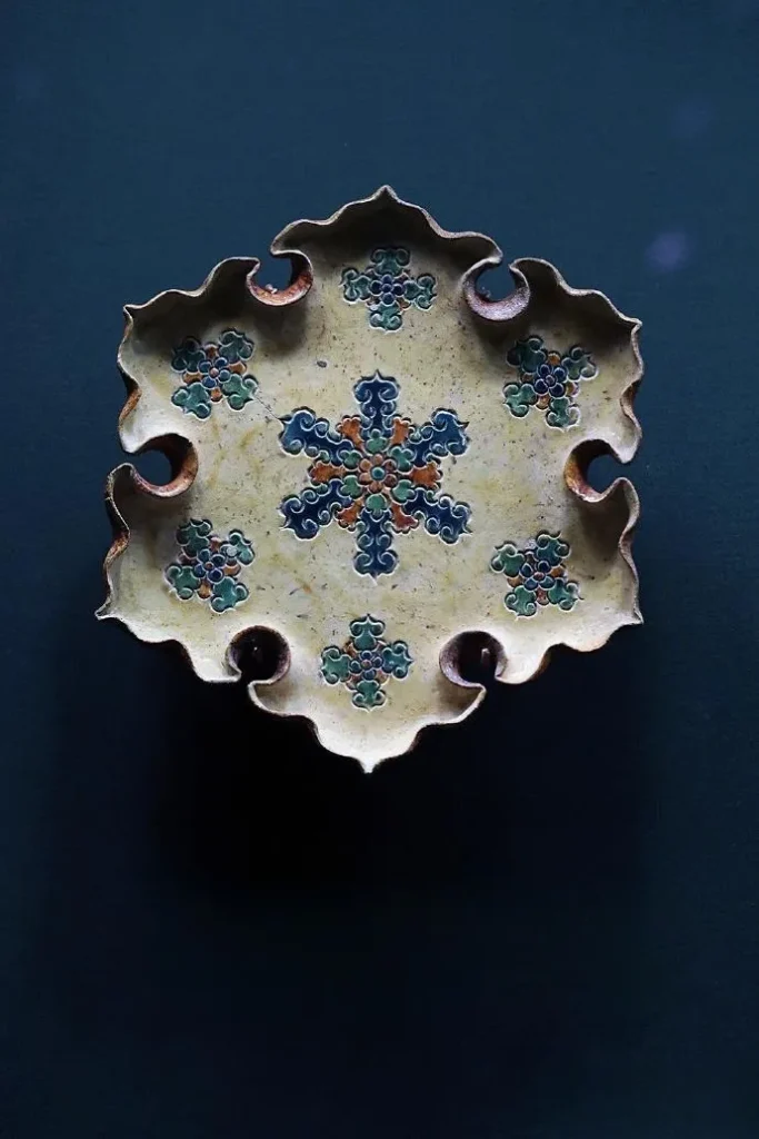 An illustration of a Tang Sancai printed lobed plate. The plate has a petal-shaped rim and is decorated with exquisite printed patterns. The glaze colors, primarily yellow, green, and white, are vibrant, showcasing the splendor and elegance of ceramic art from the flourishing Tang Dynasty.