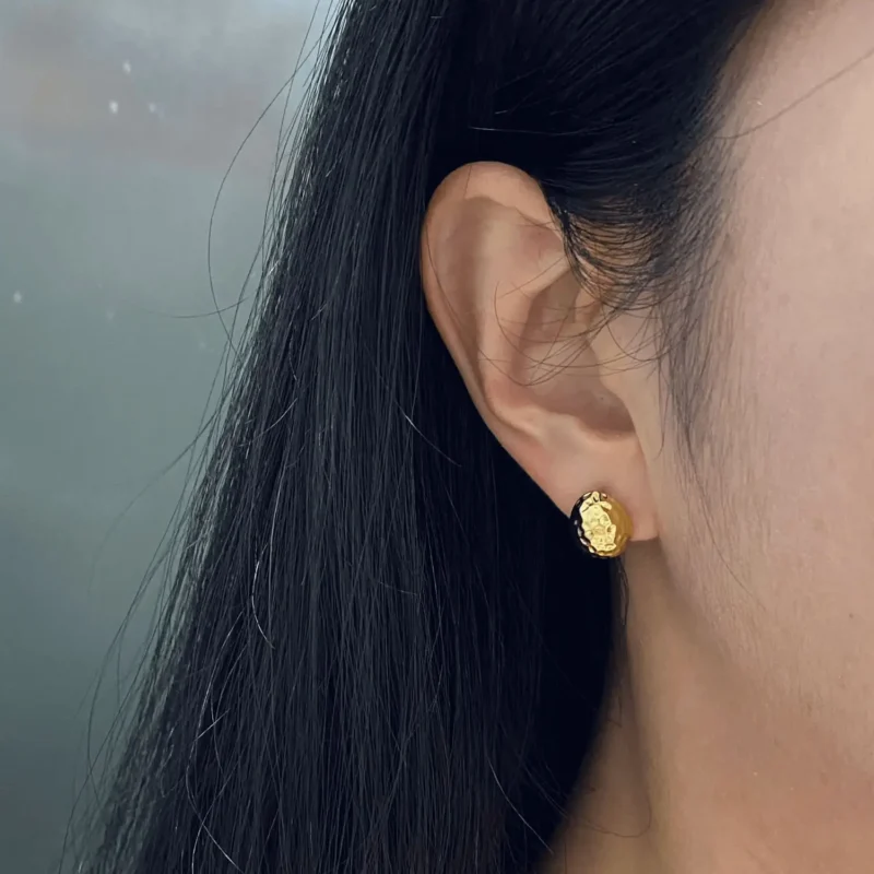 Close-up of a woman wearing gold stud earrings, showcasing their refined shine and everyday elegance.