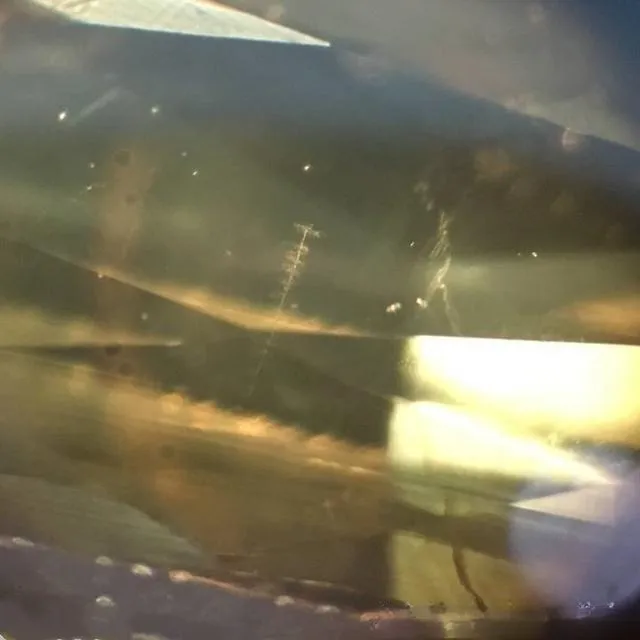 A magnified, detailed image of rutile needles inside a regular chrysoberyl gemstone. The photo clearly shows the sparse, relatively coarse needle-like crystal inclusions inside the gem, which are not sufficient to create a cat's eye effect.