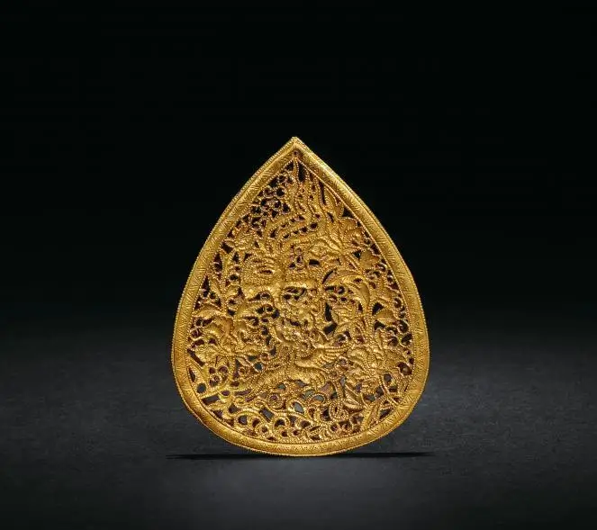 An image of a Ming Dynasty hollow-carved gold pendant. The round pendant features an intricate design of two phoenixes flying together. The delicate filigree work and the rich color of the gold are representative of noble accessories from the Ming era.