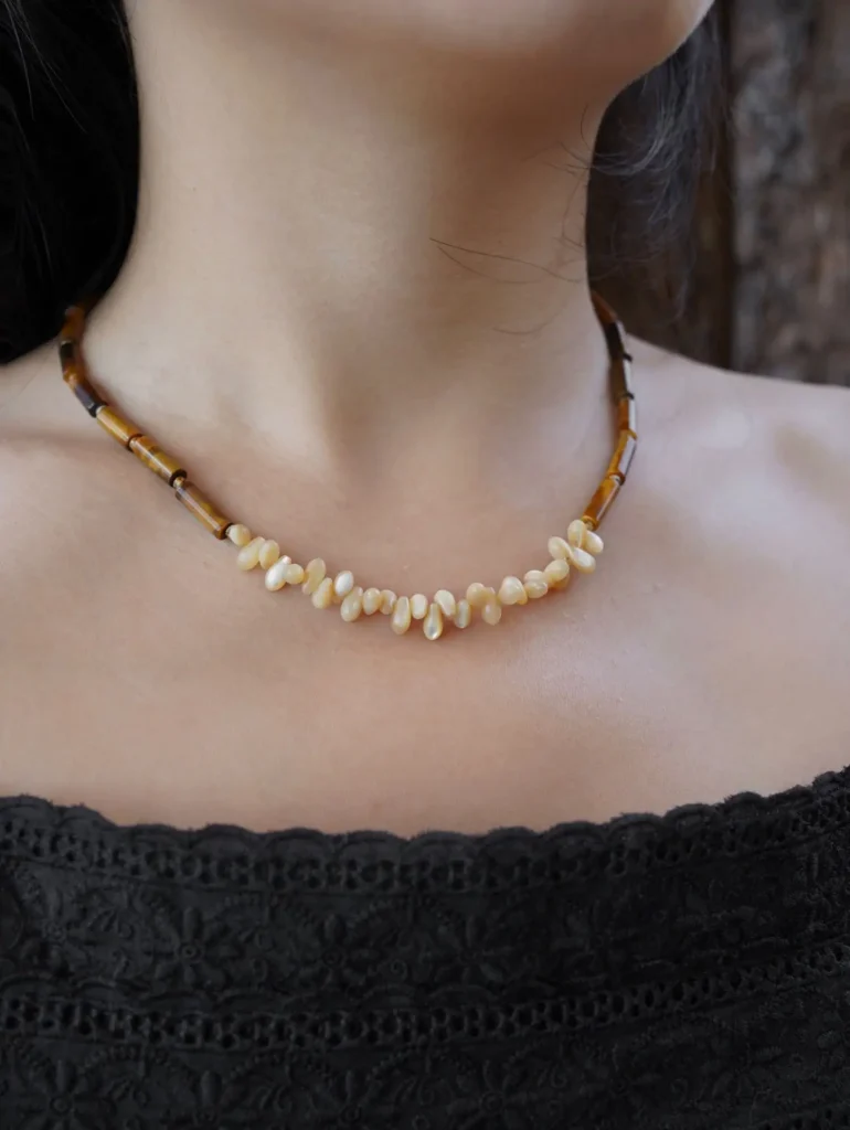 The model showcases the tiger eye and conch shell necklace, highlighting its design, texture, and everyday wearable style.