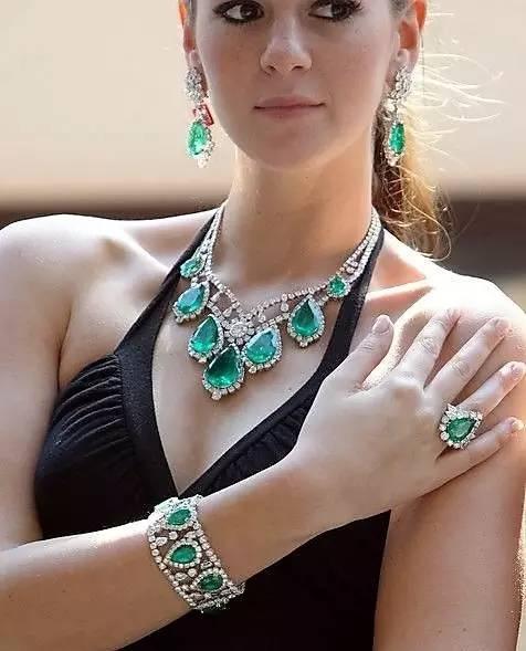 Elegant woman wearing vibrant green emerald jewelry, showcasing rings, necklaces, and earrings in a stylish ensemble