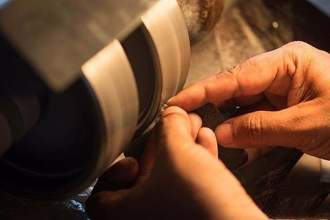Gemstone cutter shaping the rough stone on the faceting machine, removing excess material to gradually reveal the planned gemstone outline