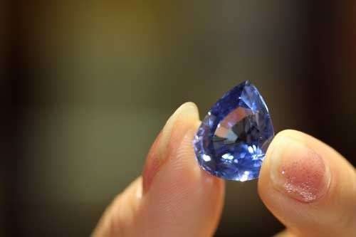 Hand holding a vibrant blue sapphire gemstone, showcasing its color, clarity, and brilliance up close.