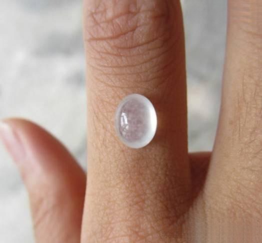 Oval jadeite cabochon held in hand, displaying natural cotton fibers inside, illustrating authentic A-jade quality and translucency.