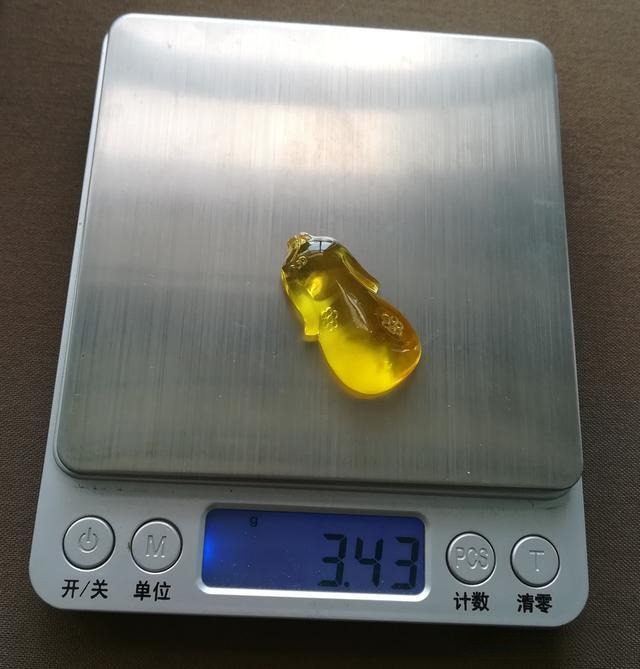 Peonyjewels custom golden beewax qipao displayed on a digital scale, highlighting the exquisite craftsmanship and weight of the gemstone-inspired design.