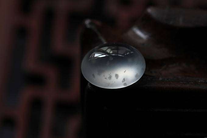 Round jadeite cabochon with cotton inclusions illuminated by light, demonstrating its clear, rigid structure and beautiful internal refraction and reflection, illustrating authentic A-jade quality.