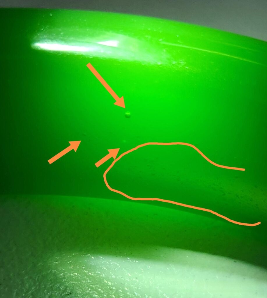 Microscopic view of an emulsified glass bangle, showing typical spherical, elongated, and tube-like bubbles found in glass imitation gemstones.