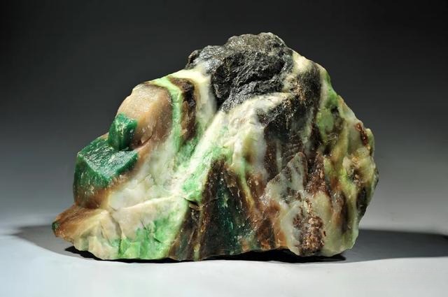 Raw jade material showing the most common mixed color palette: green, white, brown, bluish-grey, and black.