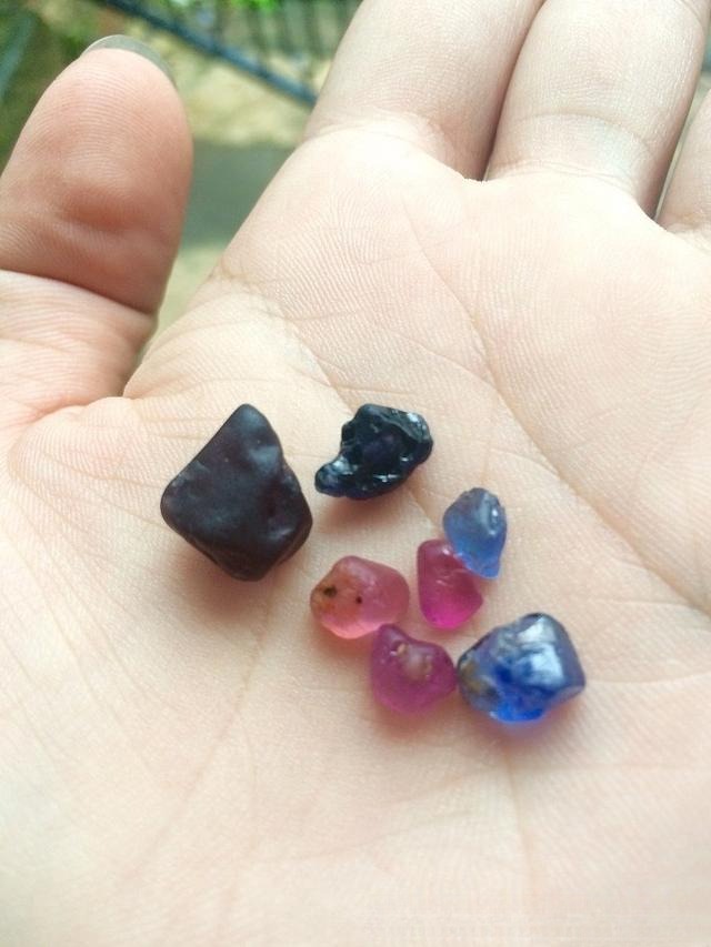 A hand displaying several cut and polished gemstones purchased at a Sri Lanka Ratnapura gem market.