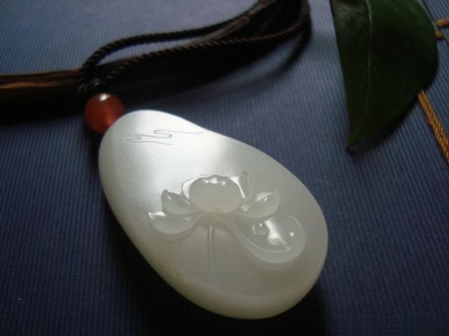 Machine-carved white jade lotus pendant with rigid lines, rough details, and fragile surface prone to cracking.