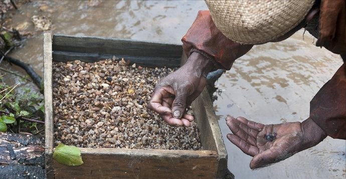 A Madagascar sapphire miner sifting river gravel, illustrating the process of finding blue sapphires in lesser known origins.
