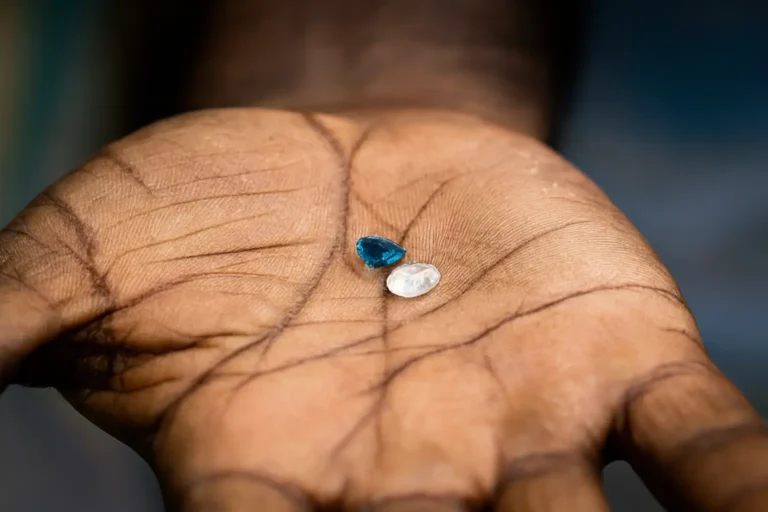 A miner's rough hand holding two natural, unpolished Ceylon Sapphire gemstones, symbolizing the raw beauty and origin of Sri Lankan gems.