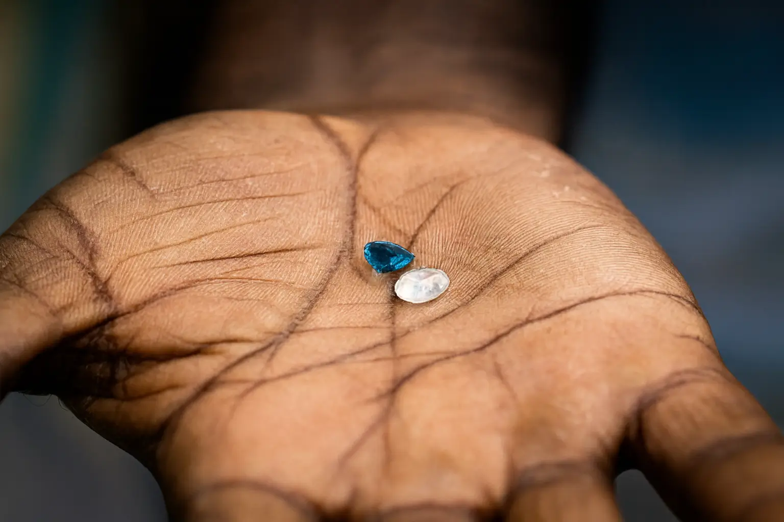A miner's rough hand holding two natural, unpolished Ceylon Sapphire gemstones, symbolizing the raw beauty and origin of Sri Lankan gems.