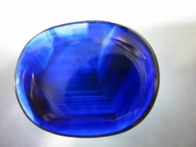 Shandong Changle "black-blue" sapphire observed under light, revealing a blue color with uneven blue zoning and distinct hexagonal growth bands inside.