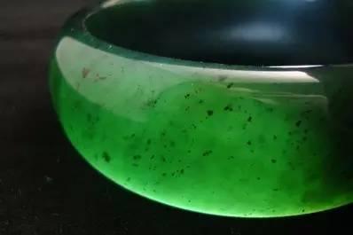 Magnified view of a Taishan Jade bangle, showing natural white and black spots typical of its serpentinite mineral composition.