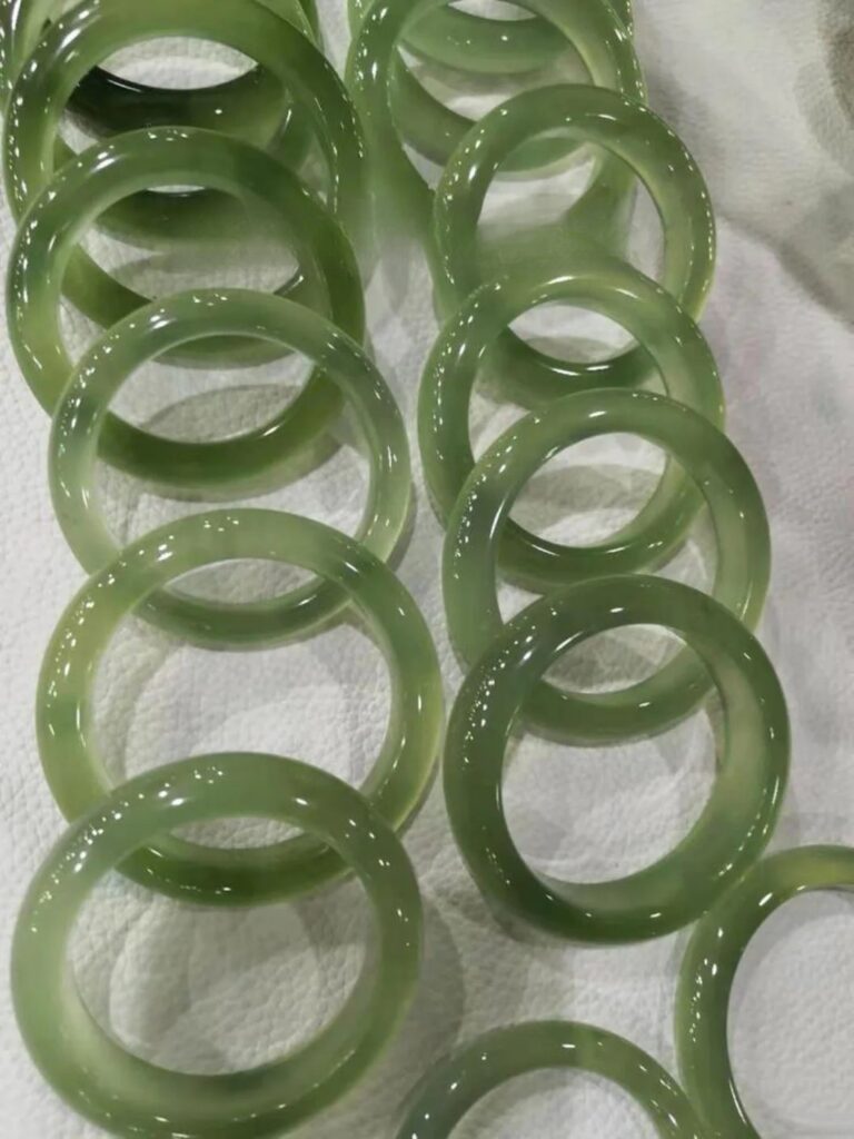A pair of Xiu Jade (Serpentine) bangles displaying their characteristic high translucency and soft, yellowish-green to bluish-green colors.