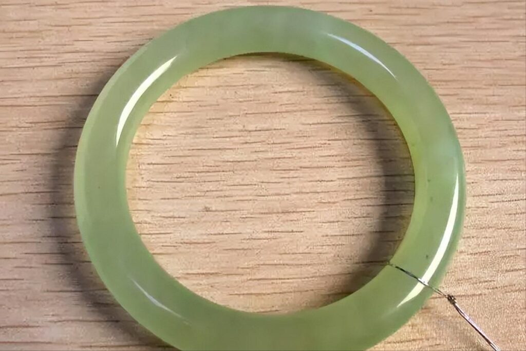 A Serpentine Jade bangle showing yellowed and dull patches, illustrating the visual degradation that occurs when wax filler ages or leaches out of surface cracks.