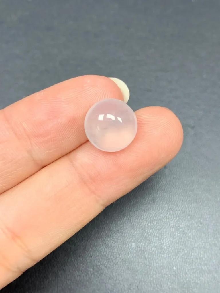 A translucent Albite (Water-Mousse Jade) cabochon showing a high degree of transparency and characteristic white inclusions.