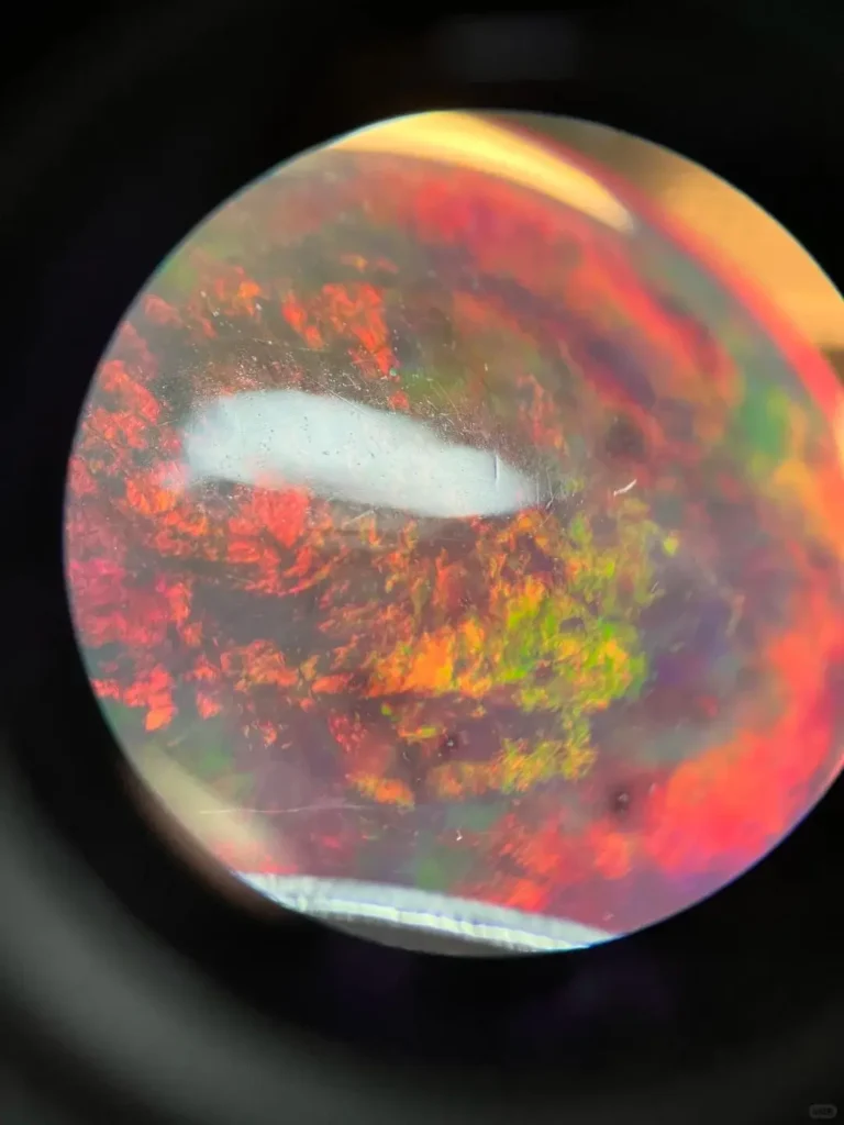 Microscopic view of dyed opal showing fragmented color patches and black carbon spots in grain boundaries.