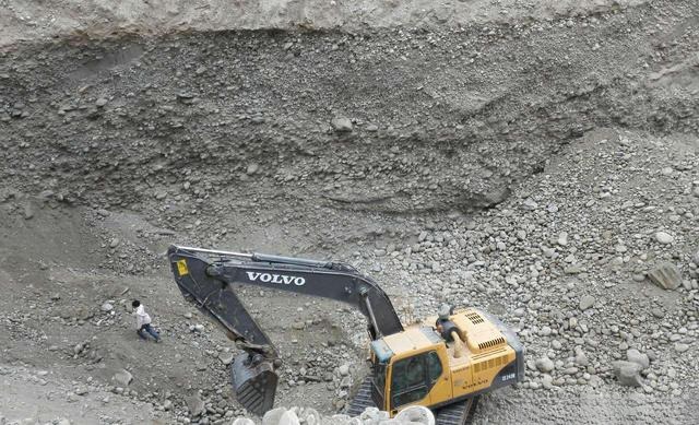 Multiple heavy excavators sifting through a dry riverbed for jade.