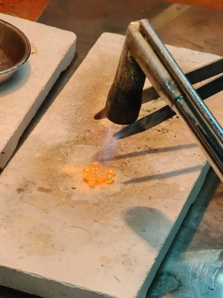 A jeweler using a professional torch to melt gold into a liquid state.