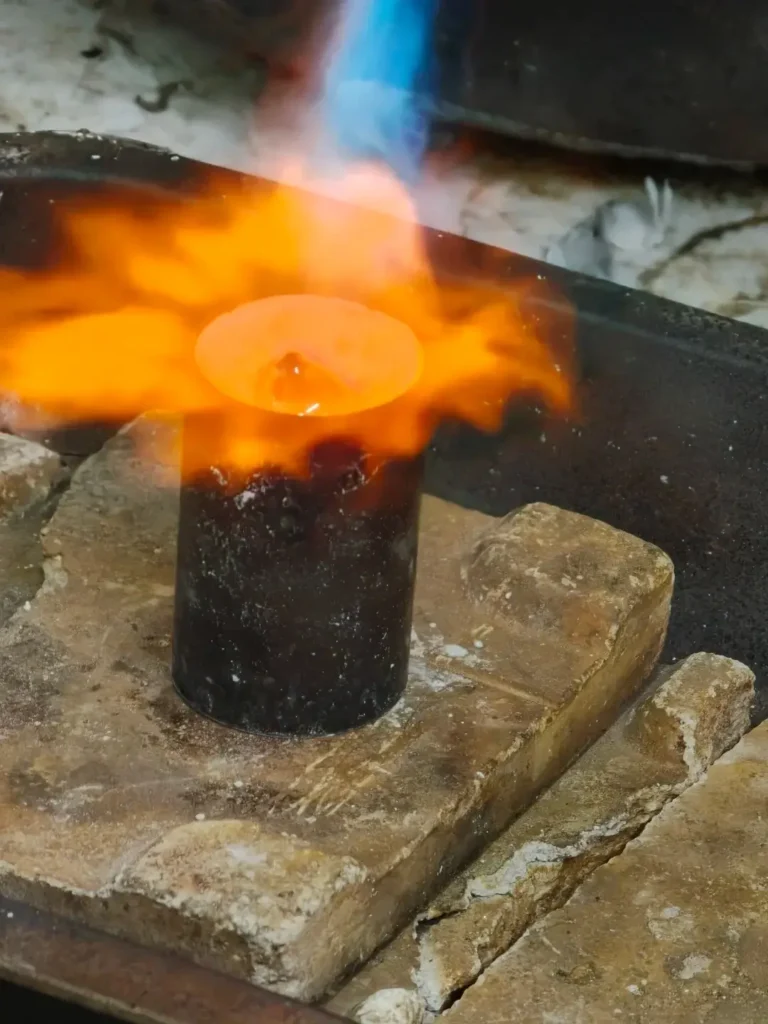 A jewelry artisan pouring molten gold into a plaster mold for casting.