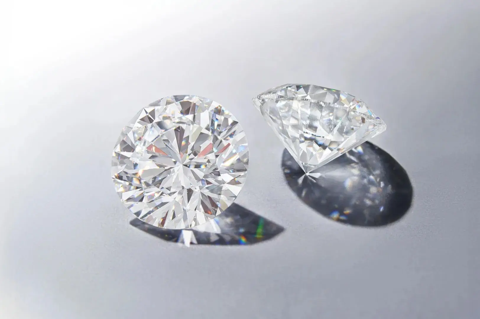 Two perfectly cut round brilliant loose diamonds, showcasing maximum brilliance and fire on a light grey background.