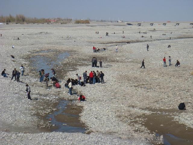 A local man searching for jade with a simple shovel on a rocky riverbank.