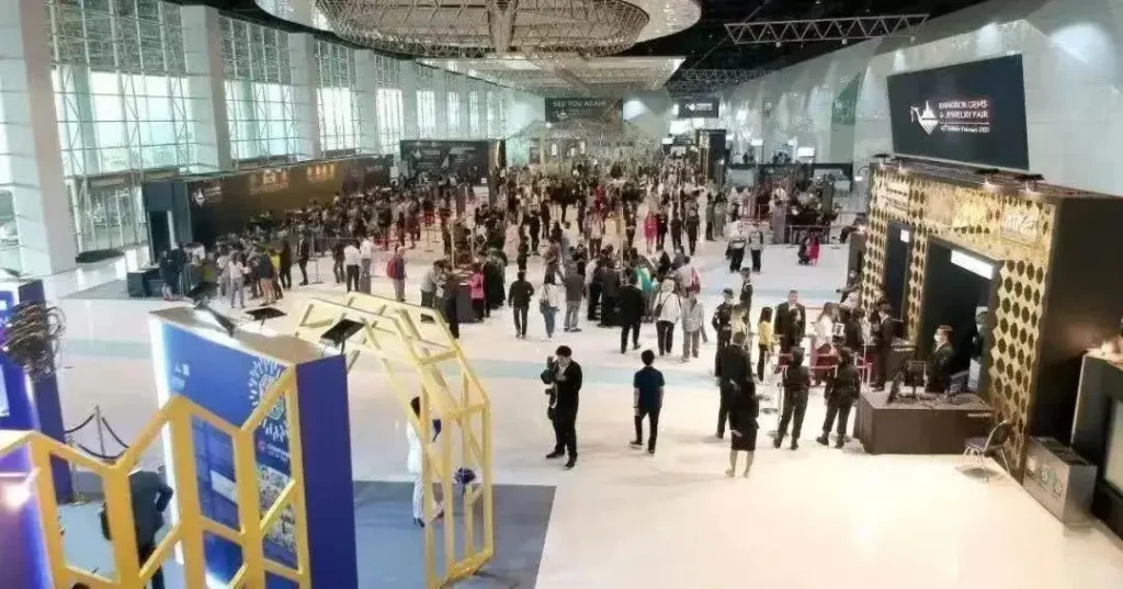 Professional buyers browsing colorful Thailand gemstones at a crowded trade booth in Bangkok.