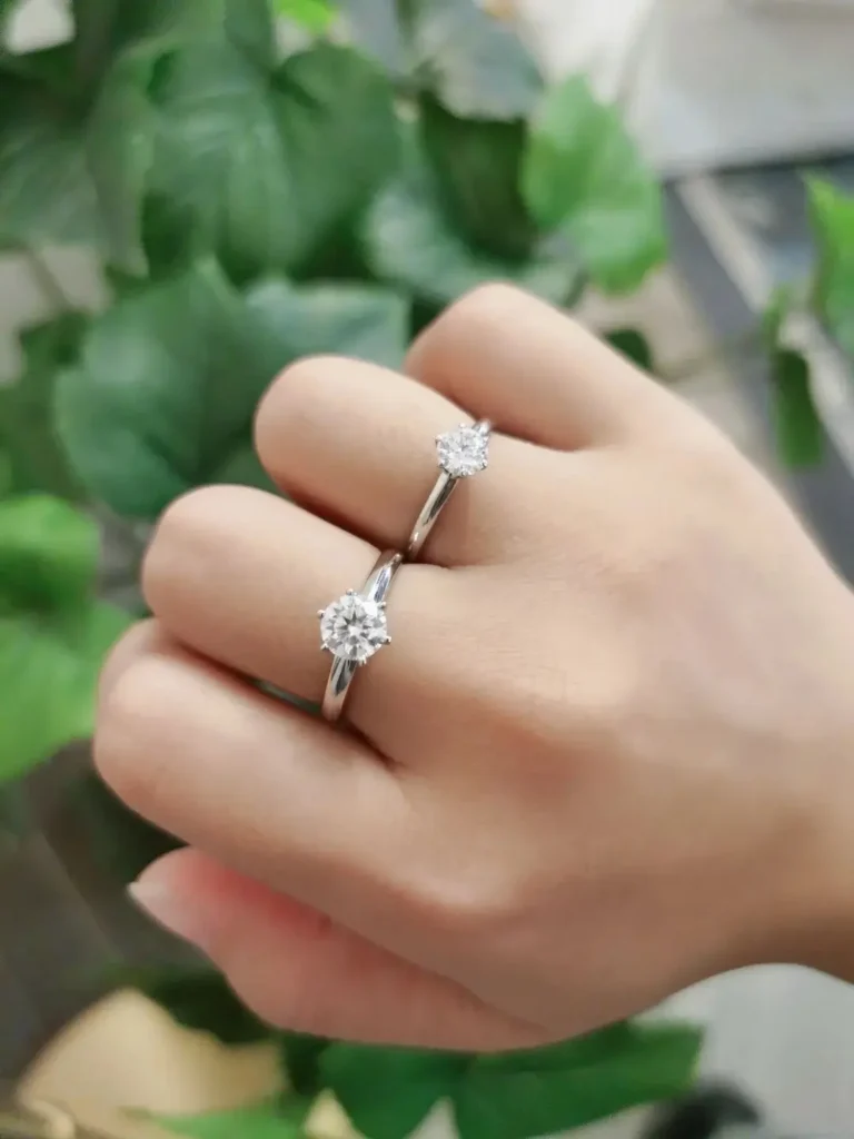 A side-by-side hand shot comparing a 1-carat Belgian Star Moissanite ring with a 0.60-carat natural diamond ring in 18K gold.