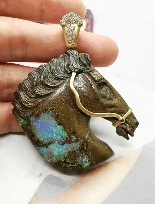 A detailed horse head sculpture carved from natural boulder opal with flashes of vibrant color.