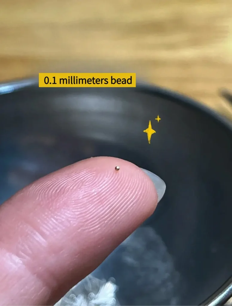 A microscopic 0.1mm gold bead placed next to a needle tip for scale.