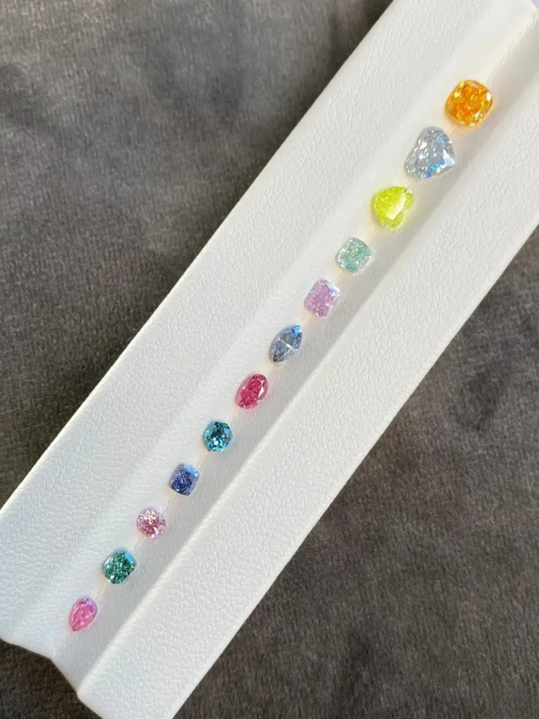 A side-by-side array of natural fancy-colored diamonds in various vivid hues including pink, yellow, and blue.