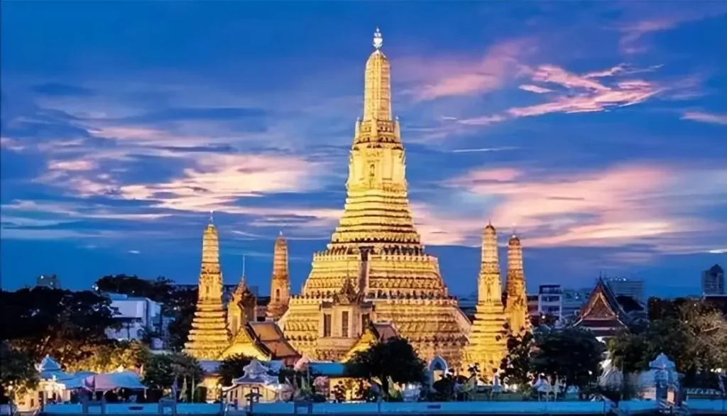 The central prang of Wat Arun decorated with colorful porcelain pieces and seashells against a blue sky.